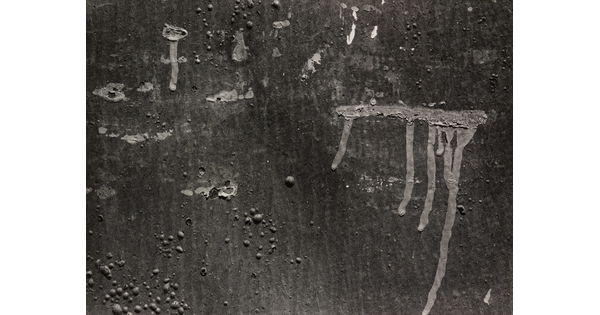 A black-and-white photograph of a close-up of paint drips on a wall.