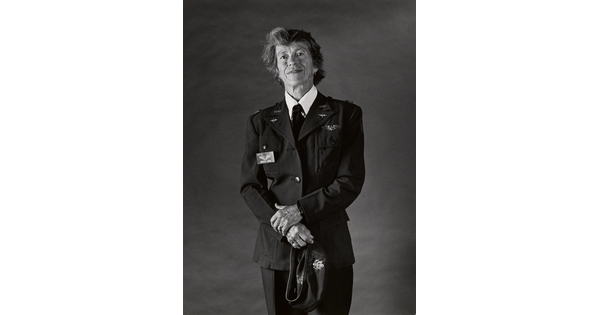 A black-and-white portrait photograph of an older White woman with short hair wearing a WASP military uniform, her hands in front of her holding a hat.