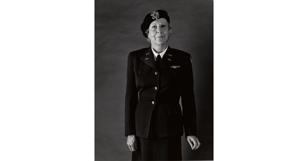 A black-and-white portrait photograph of an older White woman wearing a beret with an insignia on the front, a WASP military uniform, and holding her hands at her sides.