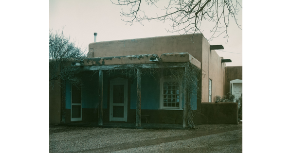 A color photograph of an adobe building with a wooden porch.