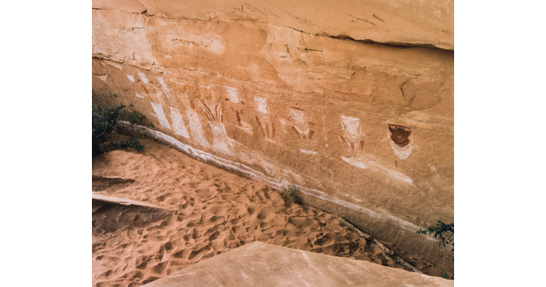 A color photograph of the base of a rock wall with petroglyphs on it.