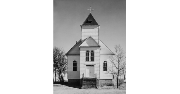 A black-and-white photograph of a white clapboard church with a cross atop the steeple.