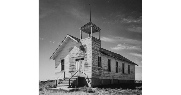 A black-and-white photograph of a white, clapboard church with peeling paint viewed at an angle.