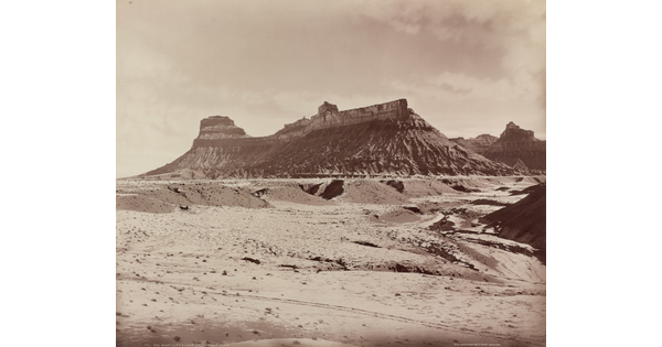 A sepia-toned photograph of a desert landscape with a rocky mesa in the distance.
