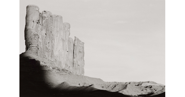 A black-and-white photograph of tall desert rock formation with a shadow encroaching from the bottom.
