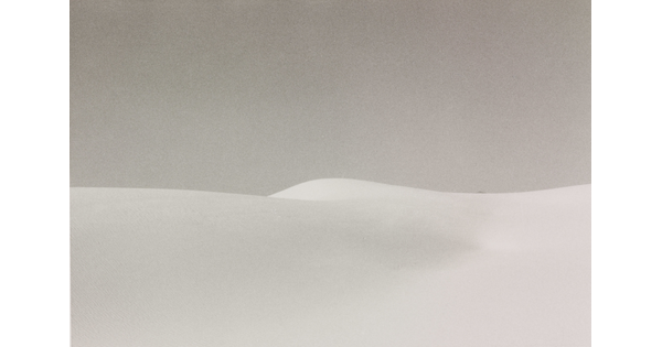 A black-and-white landscape photograph of a white sand dune against a gray sky.