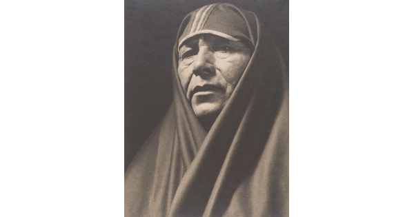 A sepia-toned portrait photograph of an adult Indigenous person with a shawl covering their head and shoulders.