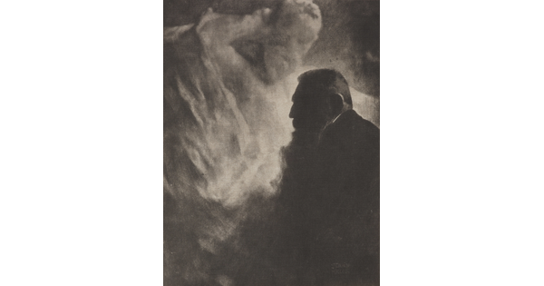 A soft-focus, black-and-white photograph of an older man with a big beard in profile against a light gray, almost smokey, background.