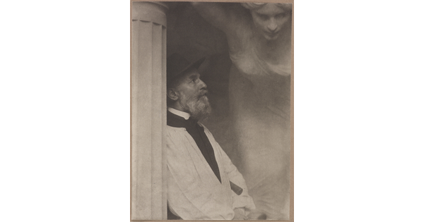 A black-and-white photograph of an older White man in profile leaning against a fluted column with what looks like a sculpture of a woman hovering over him.