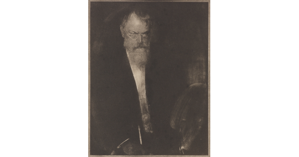 A dark, soft-focus black-and-white portrait photograph of an older White man with glasses looking down and in front of him.