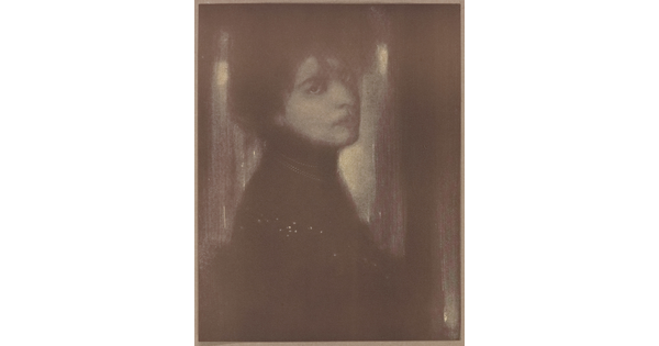 A dark, soft-focus black-and-white portrait photograph of a White woman with her hair up and head turned over her shoulder to face the camera.