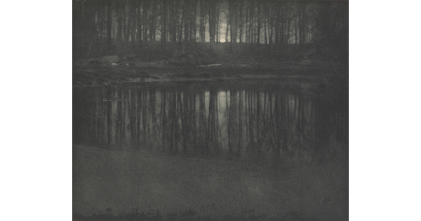 A black-and-white photograph of trees and moonlight reflected in calm water.
