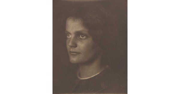 A sepia-toned portrait photograph of a young White woman, dark hair blending into the background, gazing to the side.