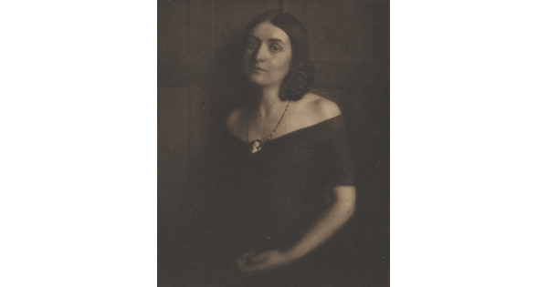 A sepia-toned portrait photograph of a young White woman wearing an off-the-shoulder dress and a cameo necklace.