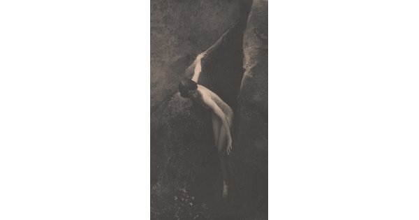 A sepia-toned photograph of a nude White woman emerging from between two large boulders.