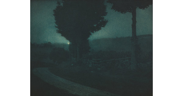 A black-and-white photograph of a tree-lined road in a dark, moonlit landscape.
