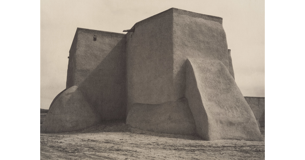 A black-and-white photograph of an adobe church from the back.