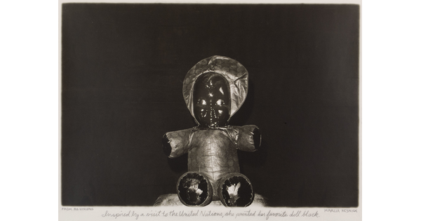 A black-and-white photograph of a seated doll with a soft body and a painted black face.