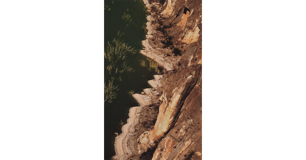 A color photograph of a landscape where a river meets a cliff face as viewed from above.