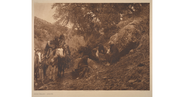 A sepia-toned photograph of a group of Indigenous people sitting on a grassy hill near their horses.