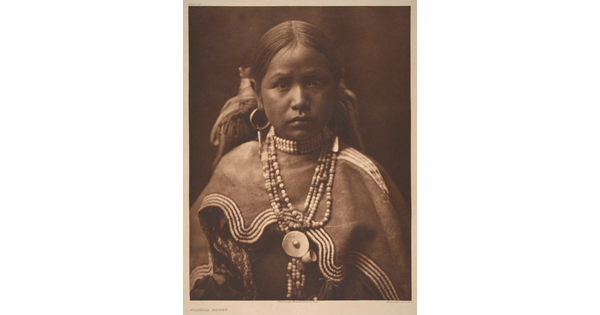 A sepia-toned portrait photograph of a young, Indigenous girl wearing a beaded necklace and cultural dress.