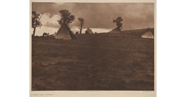 A sepia-toned photograph of a hilltop campsite with tipis amongst the scattered trees.