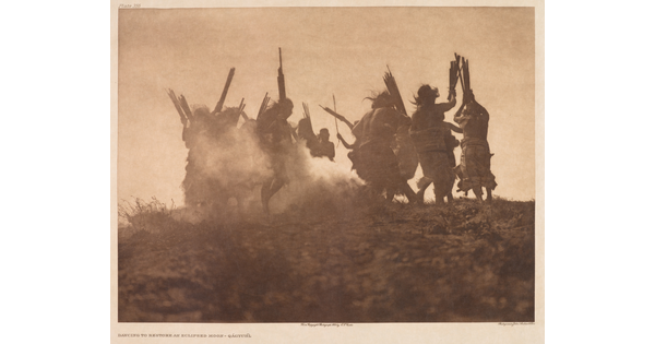 A sepia-toned photograph of the silhouettes of a group of people stirring up dust as they dance in a circle.