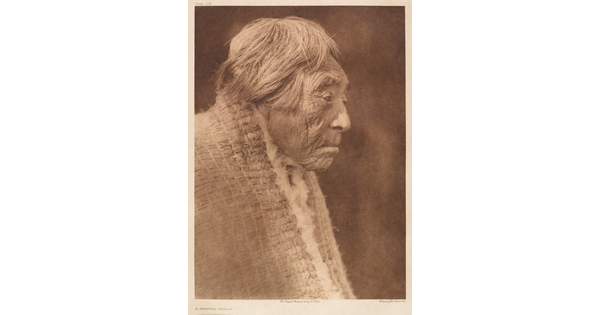 A sepia-toned portrait photograph of an elderly Indigenous woman, in profile, with short hair wearing a shawl around her shoulders.