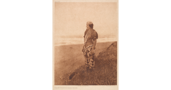 A sepia-toned photograph of a young Indigenous woman wearing traditional dress standing on a hill overlooking a plain.