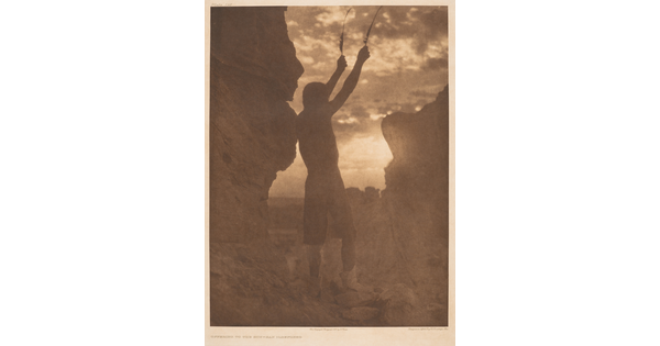 A sepia-toned photograph of a person in silhouette, arms raised in the air, standing between two large rocks.