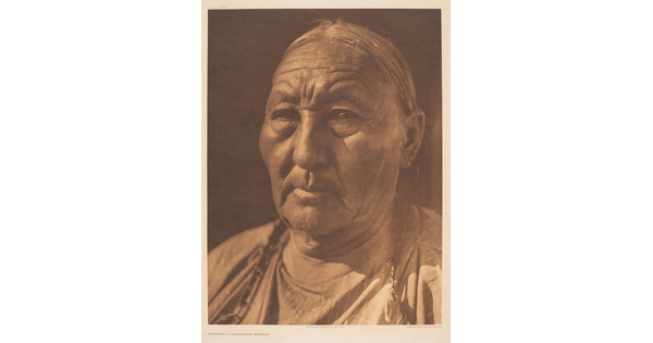 A sepia-toned portrait photograph of an older Indigenous woman with her hair in braids.