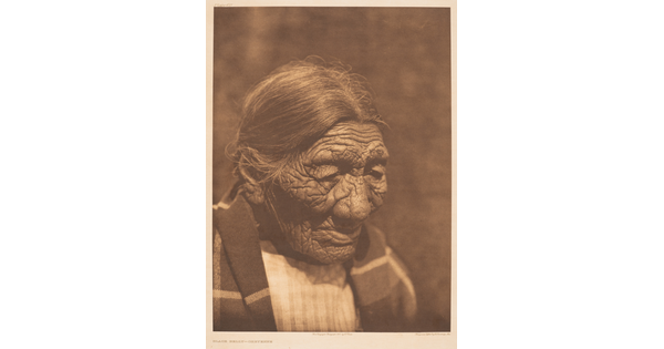 A sepia-toned photograph of an elderly Indigenous person with hair pulled back and a blanket around their shoulders.