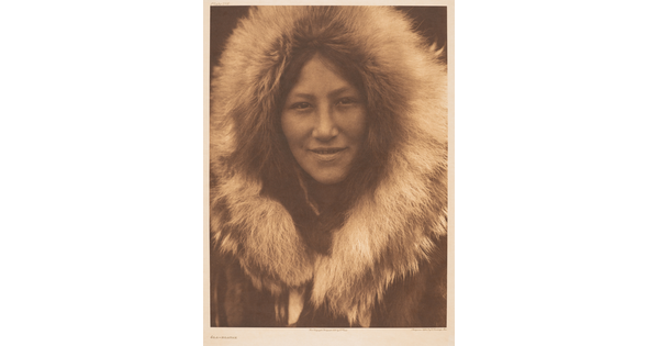 A sepia-toned portrait photograph of an Indigenous person with a fur hood framing their face.