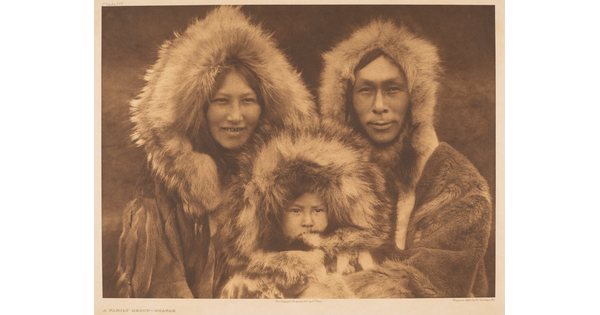 A sepia-toned portrait photograph of an Indigenous family - woman, man, and baby - all wearing furs and looking at the camera.