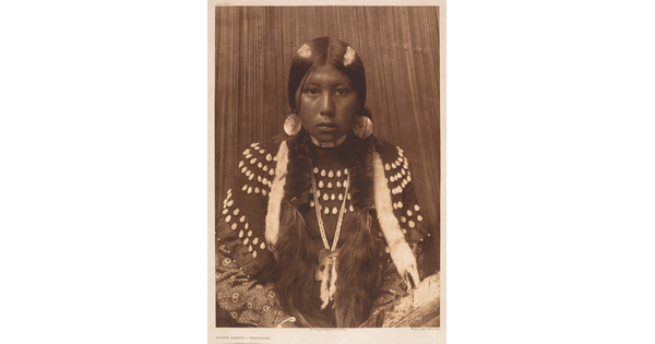 A sepia-toned portrait photograph of an Indigenous girl from the waist up dressed in traditional clothing.