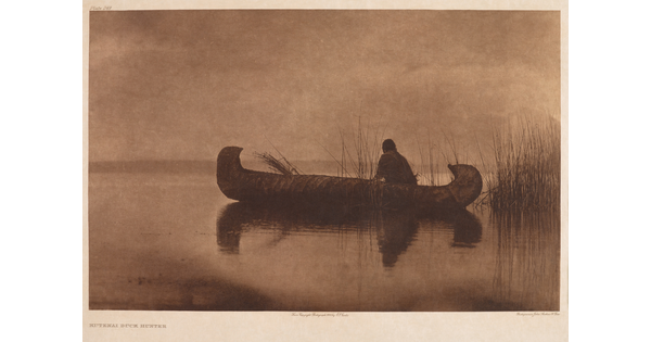 A sepia-toned photograph of an adult figure sitting in a canoe on calm water.
