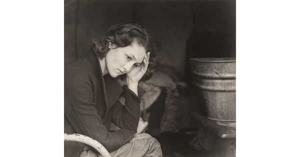 A black-and-white portrait photograph of a young, White woman sitting in a chair with her head in her hand.