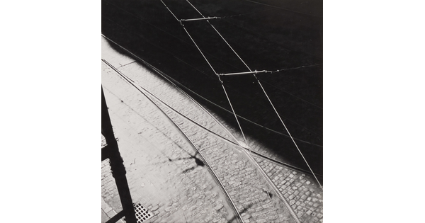 A black-and-white abstract photograph of tram tracks, a brick street, and wires divided diagonally by a hard shadow.