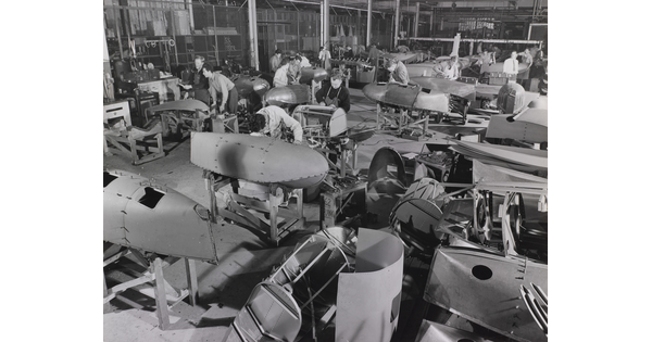 A black-and-white photograph of adult workers in an aircraft factory manufacturing aircraft parts.
