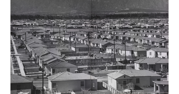 A black-and-white photograph of a sprawling suburb of ranch-style houses with mountains in the distance.