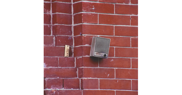 A color photograph of a doorbell and an intercom on a red brick wall.