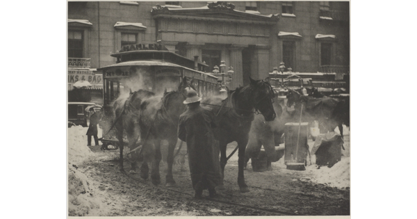 A black-and-white photograph of horses pulling a trolley on a busy street covered with slush and snow.