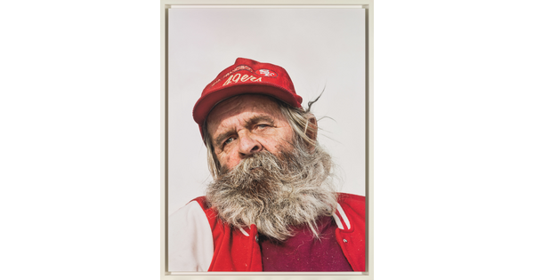 A color photograph of an older White man with a scraggly gray beard wearing a red 49ers hat and a red jacket.