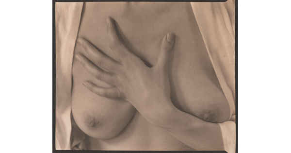A sepia-toned photograph of the torso of a White woman with her hand on her bare chest between her breasts.