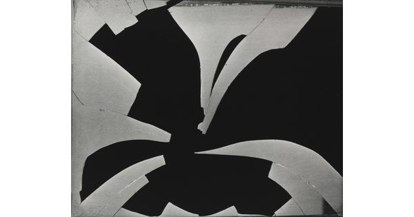 A black-and-white photograph of a pane of broken glass with many pieces missing in front of a black background.