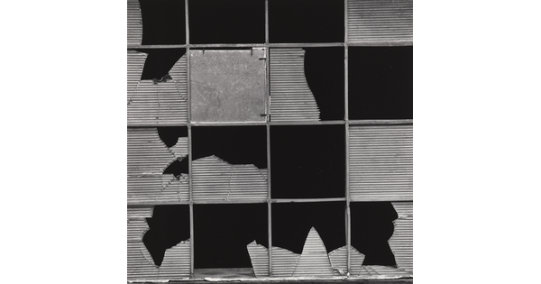 A black-and-white photograph of a metal grid with broken or missing textured glass pieces in each section.