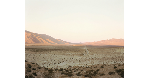 A color photograph of a desert landscape with sunlight reflecting off distant mountains.