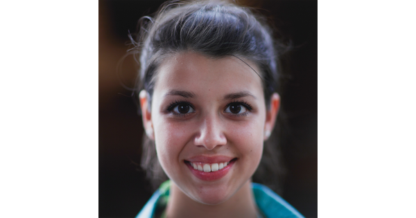 A color photograph of the face of a young, smiling White woman with dark hair pulled back from her face.