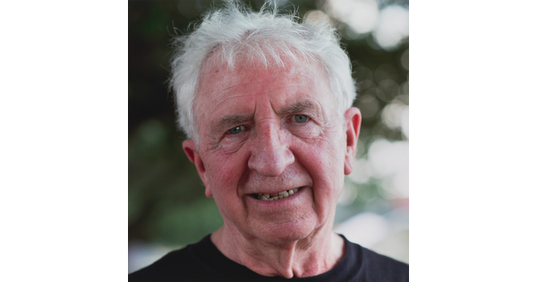A color photograph of the head and shoulders of a smiling older White man with white tousled hair.