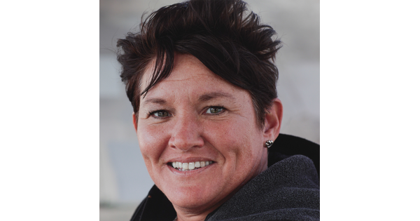 A color photograph of a smiling White woman with dimples, short, dark hair, earrings, wearing what looks like a hoodie.